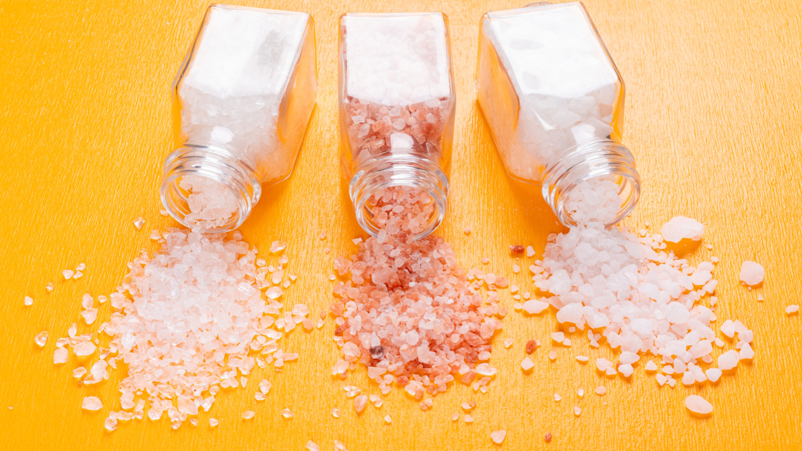 Some sea salt with himalayan salt coming out of salt shaker on orange background, close-up.