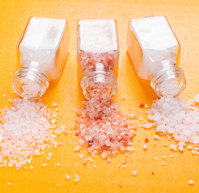 Some sea salt with himalayan salt coming out of salt shaker on orange background, close-up.